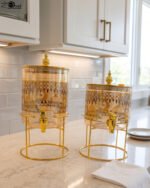Amber tinted glass beverage dispenser with intricate Islamic mosque gold pattern on a metal stand.