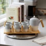 A stylish ceramic tea set in grey and white with wooden-style handles, consisting of six cups and one kettle, neatly arranged on a wooden tray display.