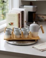 A stylish ceramic tea set in grey and white with wooden-style handles, consisting of six cups and one kettle, neatly arranged on a wooden tray display.