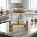 6.5-liter clear glass beverage dispenser with a gold spigot set on a raised wooden stand on a marble countertop