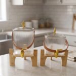 Ribbed glass beverage dispenser with leather carrying handle and gold spigot set on a wooden stand