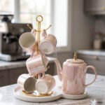 Luxury iridescent ceramic tea set with 6 cups, kettle, white ceramic tray, and golden display stand on a kitchen counter.