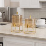 Two amber fluted glass beverage dispensers on gold metal stands resting on a modern kitchen counter