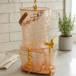 Elegant pink acrylic beverage dispenser with gold swan finial, gold spigot, stand, and 6 matching diamond-cut glasses.