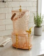 Elegant pink acrylic beverage dispenser with gold swan finial, gold spigot, stand, and 6 matching diamond-cut glasses.