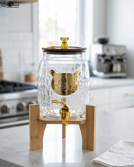 3.6-liter clear glass drink dispenser featuring a gold bear face design, gold spigot, and sturdy wooden stand set on a kitchen counter
