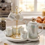 Luxurious iridescent ceramic tea set featuring six cups, one kettle, and a gold-finish stand on a white tray, arranged on a marble kitchen counter.