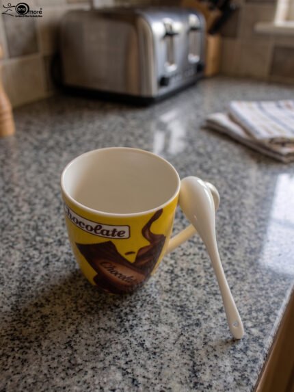 Yellow ceramic chocolate mug with handle holding a matching white spoon on a granite countertop