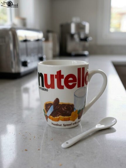 White ceramic coffee mug printed with Nutella hazelnut spread logo and toast graphics resting on a kitchen counter next to a white spoon.