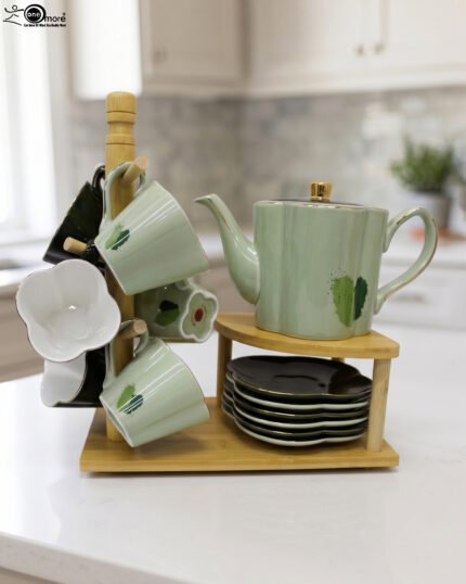 Green and black ceramic tea set with 6 cups, kettle, saucers, and a wooden display stand on a kitchen counter