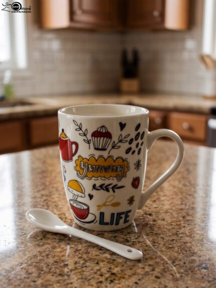 White ceramic coffee mug with colorful coffee and dessert doodle illustrations paired with a small ceramic spoon on a kitchen counter.