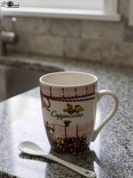 Vintage-style ceramic cappuccino mug with printed coffee beans and vintage coffee grinder, placed next to a small white ceramic spoon on a granite countertop.