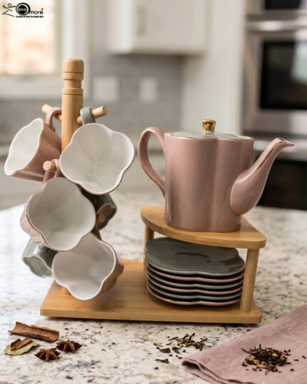 Pink and pastel ceramic tea set featuring 6 cups, 1 kettle, and a stacked saucer tier organized on a wooden display stand and tray on a kitchen counter.