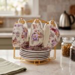Luxury floral ceramic tea cups and saucers neatly organized on a golden storage stand on a kitchen counter.