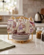 Luxury floral ceramic tea cups and saucers neatly organized on a golden storage stand on a kitchen counter.