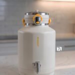 Off-white 7-liter insulated water cooler dispenser with spigot tap and stainless steel lid on a kitchen counter