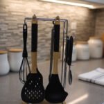 8 piece black silicone kitchen utensil set with wooden handles hanging on a chrome stand