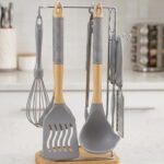 8 pcs grey silicone cooking utensils set with wooden handles hanging on a stainless steel stand with wooden base