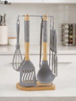 8 pcs grey silicone cooking utensils set with wooden handles hanging on a stainless steel stand with wooden base