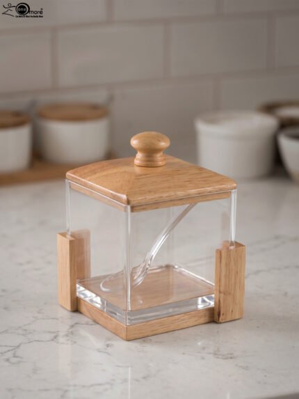 Square clear acrylic sugar pot with a natural wooden lid, clear serving spoon, and wooden base stand on a kitchen countertop.