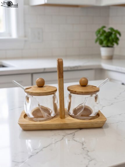 Two clear acrylic condiment jars with wooden lids and glass spoons set on a wooden stand tray with handle on a white marble countertop.