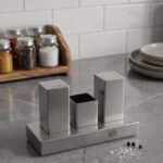 Brushed stainless steel rectangular salt and pepper shaker set with center holder on a matching metal base tray.