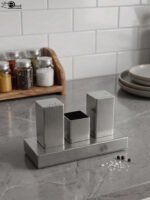 Brushed stainless steel rectangular salt and pepper shaker set with center holder on a matching metal base tray.