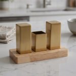 Modern brushed gold stainless steel salt and pepper shaker set with toothpick holder in a wooden base on a kitchen counter
