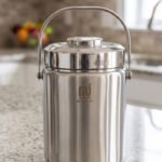 Polished insulated stainless steel lunch box container with a metal carrying handle on a kitchen countertop