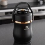 Matte black portable insulated lunch box jar with gold trim accent and black top handle on a kitchen counter