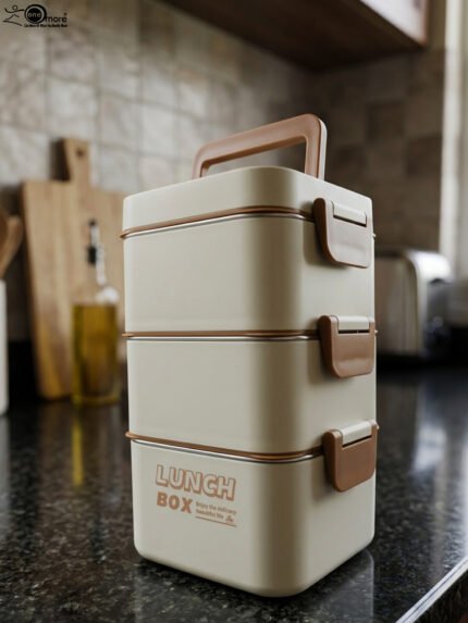 Cream and brown 3-tier stackable stainless steel lunch box with carrying handle on a kitchen counter
