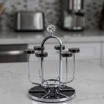 Modern silver chrome glass stand with crystal top finial holding six inverted glasses on a kitchen countertop.