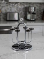 Modern silver chrome glass stand with crystal top finial holding six inverted glasses on a kitchen countertop.