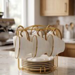 White ceramic tea cups and saucers neatly organized on a luxury golden stand on a marble kitchen countertop.