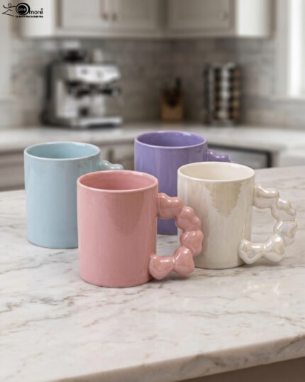Four colorful ceramic mugs with unique bubble-textured handles arranged on a marble kitchen countertop.