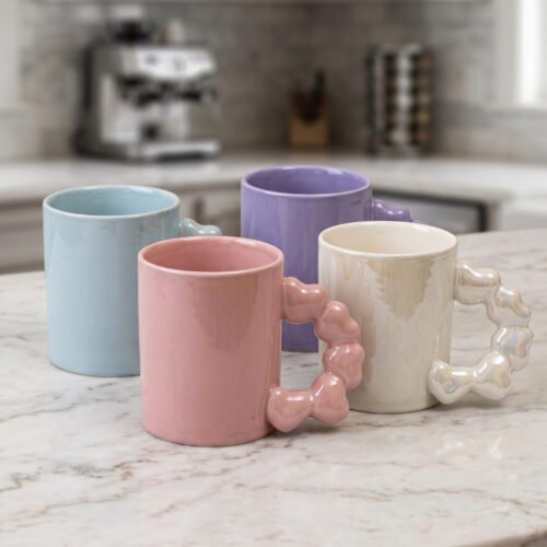 Four colorful ceramic mugs with unique bubble-textured handles arranged on a marble kitchen countertop.