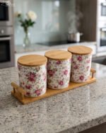 Three floral print ceramic storage jars with bamboo lids arranged on a matching wooden tray on a modern kitchen countertop