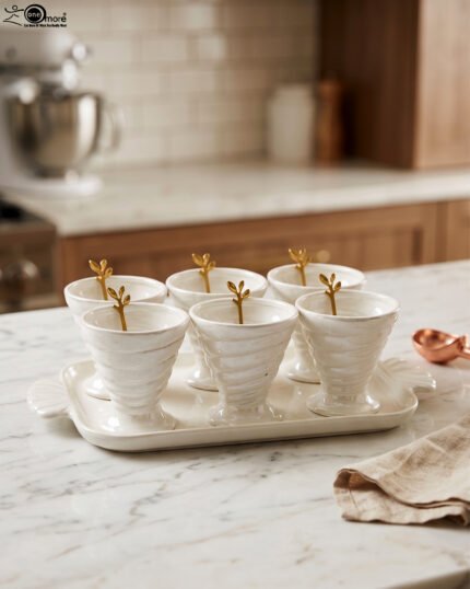 White ceramic ice cream set with 6 swirled pedestal bowls, matching serving tray, and gold leaf spoons displayed on a marble kitchen counter.