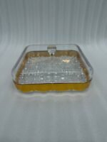 Two square crystal dry fruit dishes with gold trim bases and glass lids displayed on a wooden table in a luxury living room setting.