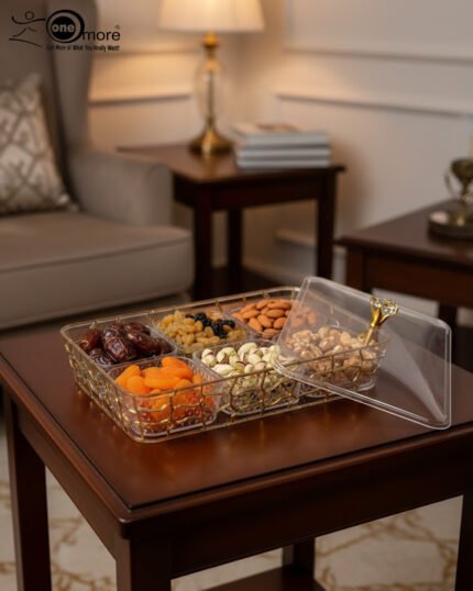 Clear acrylic dry fruit serving tray with gold-toned wire compartments, a matching lid, and filled with assorted nuts and dried fruits on a wooden table.