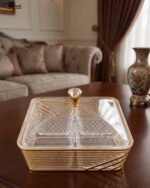 Two luxury clear acrylic dry fruit serving dishes with gold trim, crystal knobs, and partitioned compartments displayed on a modern wooden coffee table.