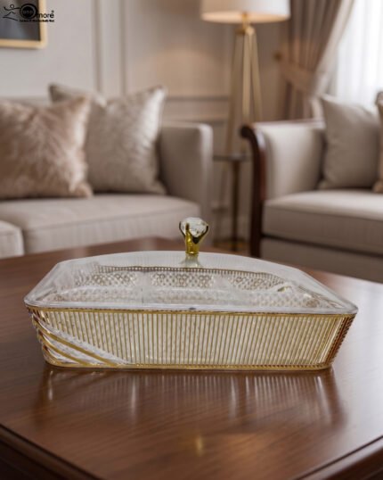 Elegant partitioned glass dry fruit dish with a gold trim and crystal-accented lid sitting on a wooden coffee table in a modern living room.