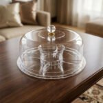 Clear acrylic dry fruit and cake serving platter with multi-compartments, center bowl, and a crystal knob dome lid resting on a wooden table.