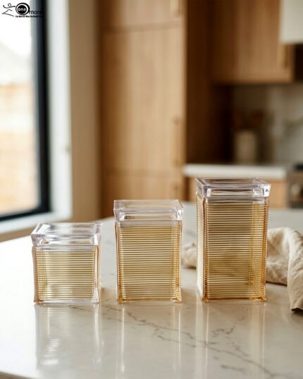 Three varying heights of clear ribbed acrylic storage jars with lids arranged on a modern kitchen countertop.