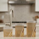 A set of three clear acrylic storage jars with decorative ribbed gold detailing, displayed neatly on a modern kitchen countertop.