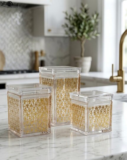 Set of three clear acrylic kitchen storage jars with elegant gold patterned designs, displayed on a marble countertop.