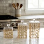 A luxury 3-piece clear acrylic jar set with gold geometric patterns and crystal lids, neatly arranged on a white marble kitchen countertop.