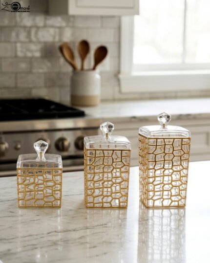 A luxury 3-piece clear acrylic jar set with gold geometric patterns and crystal lids, neatly arranged on a white marble kitchen countertop.