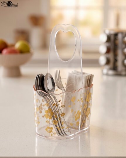 Clear acrylic spoon and cutlery holder featuring a gold floral design, divided compartments holding silverware and napkins, and a heart-shaped handle on a kitchen countertop