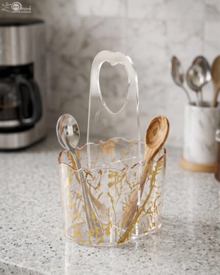 Clear acrylic spoon holder and cutlery caddy with gold accent patterns and a heart-shaped handle on a kitchen countertop holding utensils.